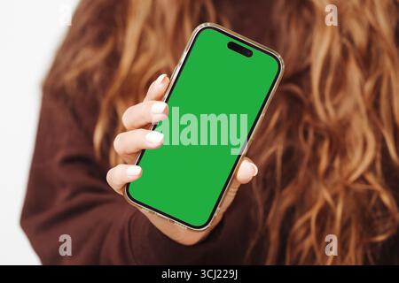 Woman holding smartphone. Green screen mobile phone in hand. Technology and communication concept. Blank display for mockup design. Stock Photo
