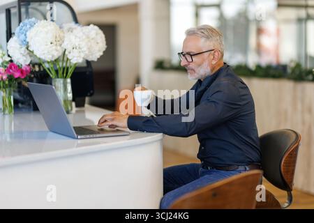 Thoughtful businessman drinking coffee, looking through window at big modern city, having break, deep in thoughts, enjoying view, waiting for meeting Stock Photo