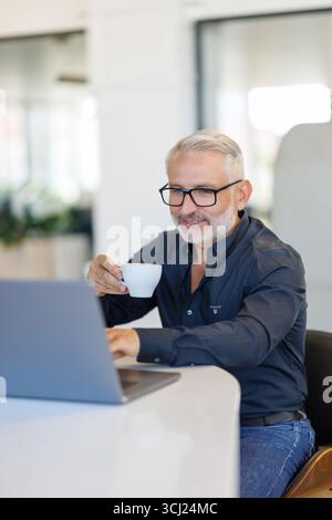 Thoughtful businessman drinking coffee, looking through window at big modern city, having break, deep in thoughts, enjoying view, waiting for meeting Stock Photo