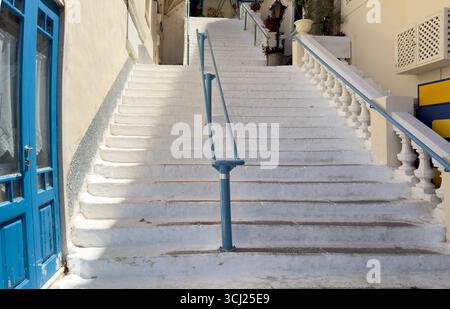 Whitewashed stone staircase with blue railings leading between traditional houses in Poros town, Greece, blue summer sky. Stock Photo