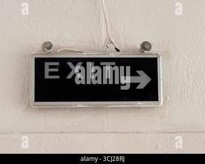 Exit sign with white letters and arrow on black background fixed to wall. Navigation, safety and communication represented through signage, typography Stock Photo