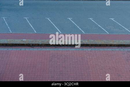 Top view of an empty parking lot with white parking space markings, stone border, and red brick pavement. Stock Photo