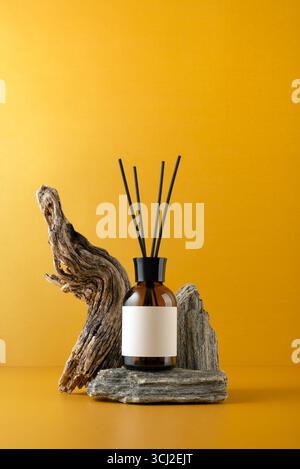 Aroma diffuser in brown glass bottle on stone podium with sticks, driftwood and on orange background, minimalist still life with natural textures and Stock Photo