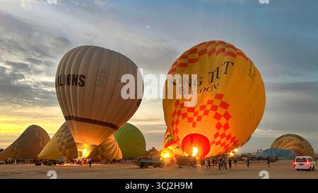 Luxor, Egypt - Feb 10, 2025: Colorful hot air balloons being inflated before sunrise, with flames lighting the scene and tourists preparing for flight Stock Photo