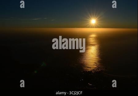 A sunset over the horizon. The rich hues of the sky are reflected in the calm water below. Cape Town, South Africa (Photo by Chris Ricco) Stock Photo