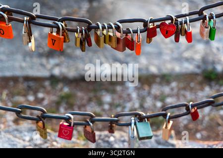 Colorful love padlocks hanging on metal chain. Various colorful padlocks, symbolizing love and commitment, hang from a metal chain outdoors as part of Stock Photo
