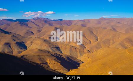 Sweeping view of arid Moroccan mountain ridges, their wavy formations highlighted by sunlight and stretching endlessly beneath a deep blue sky Stock Photo