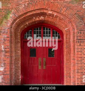 Gothic arched red double doors with small windows set in a historic brick church facade in Chicago. Stock Photo