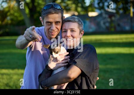 A smiling couple enjoys a sunny day outdoors while holding their Canadian Sphynx cat in a park. The image reflects affection, companionship, and the w Stock Photo