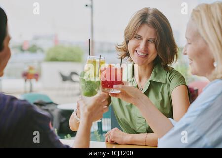 Middle Aged Women Smiling While Toasting Colorful Drinks Outdoors Stock Photo
