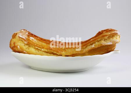 Eclair filled with pastry cream on a ceramic plate Stock Photo