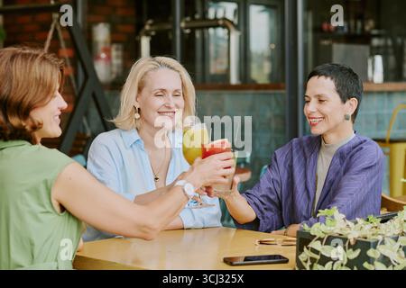 Three Middle Aged Women Smiling While Toasting with Cocktails Stock Photo