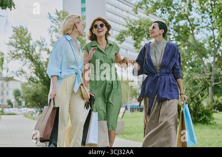 Three Middle Aged Women Laughing While Walking with Shopping Bags Stock Photo