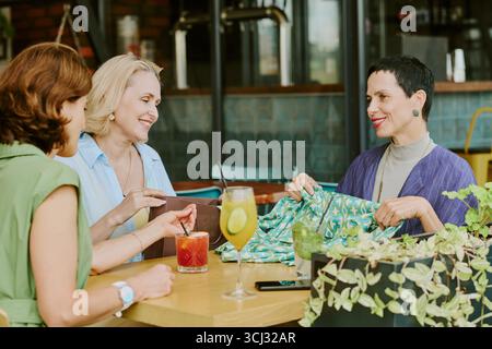 Three Middle Aged Women Socializing and Smiling at Restaurant Table Stock Photo