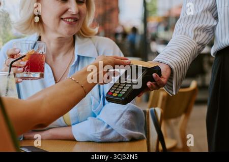 Middle Aged Woman Making Contactless Payment at Restaurant Table Stock Photo