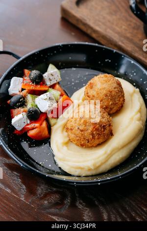 Mashed potatoes with crispy cutlets and fresh Greek salad on a black rustic plate Stock Photo