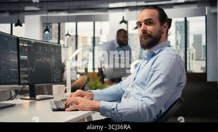 Close up of happy trader in prop firm workplace analyzing market data and executing trades using trading software interface on PC. Joyous stockbroker at work monitoring stock prices Stock Photo