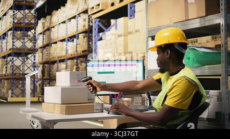 Black staff member using a barcode scanner to process shipping labels on boxes from industrial storage racks. Scanning awb tags for package tracking service and accurate logistics. Camera A. Stock Photo