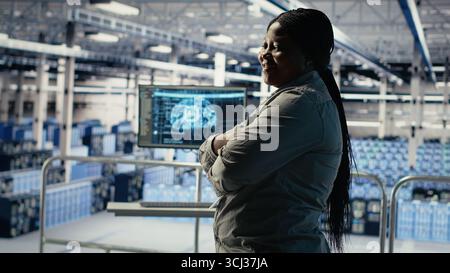 Portrait of smiling IT professional in server farm optimizing machine learning systems handling tasks. Happy data center female engineer adjusting neural networks AI model parameters, camera B Stock Photo