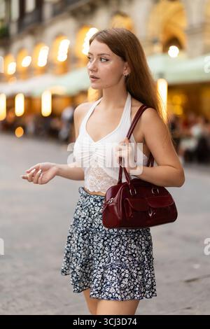 Woman in summer dress walks along the evening street of Barcelona against the backdrop of cafes and restaurants with romantic lighting Stock Photo