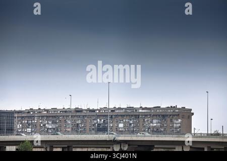 Long, grey socialist-era apartment slab looms beyond an elevated highway under a heavy sky, rows of identical windows stressing brutalist mass housing Stock Photo