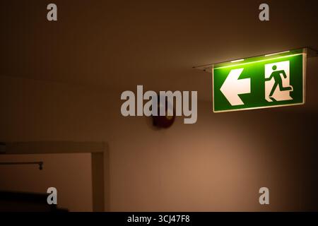 Exit way out arrow direction, Escape guidance sign green color light emergency exit sign in a dark room installation at ceiling building hallway corri Stock Photo