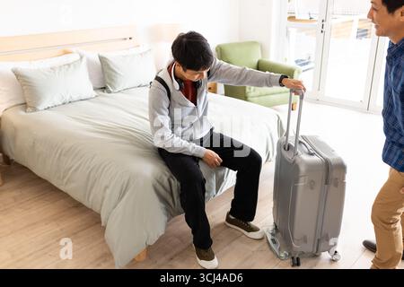 Young man sitting on bed with suitcase, preparing for travel at home Stock Photo