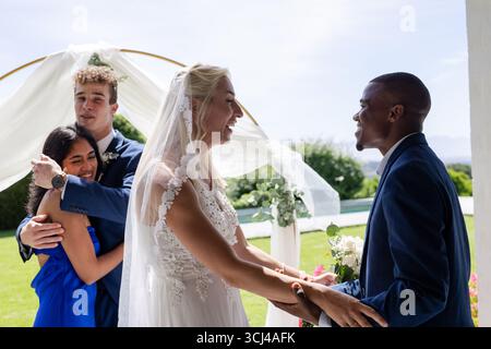 Celebrating at outdoor wedding, bride and groom smiling joyfully with friends Stock Photo