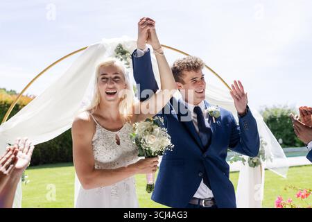 Bride and groom celebrating outdoors, holding hands and smiling joyfully Stock Photo