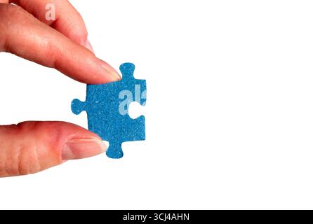 A hand holding a puzzle piece. Female fingers with a blue jigsaw puzzle piece. Stock Photo