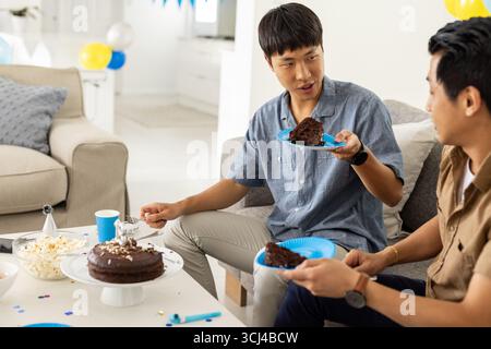 Friends enjoying chocolate cake and conversation at home during casual gathering Stock Photo