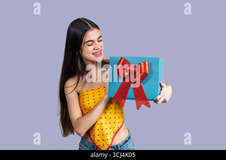 Smiling young woman with braces holding a blue gift box with a red bow, expressing joy and excitement Stock Photo