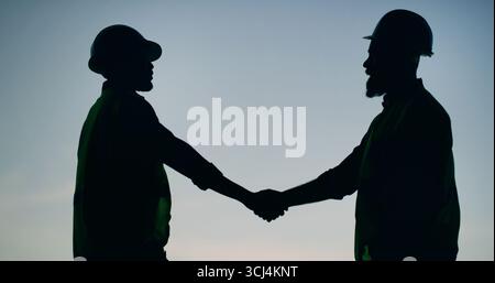 Silhouette, handshake and men in outdoor with hard hats, partnership or agreement for project plan. Team, shaking hands and construction at sunset Stock Photo