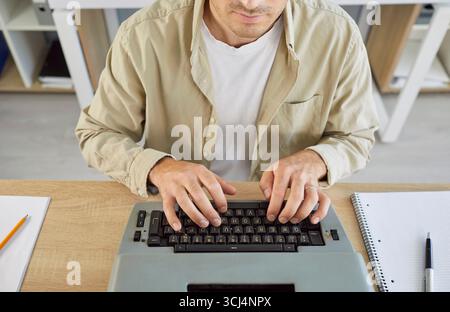 Man typing on laptop keyboard at desk, overhead home office scene with notepad Stock Photo