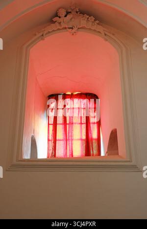 Red curtain on an ornate window of an Italian monastery with light coming in Stock Photo