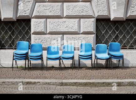 empty blue chairs on the sidewalk against the wall of a building after an event Stock Photo