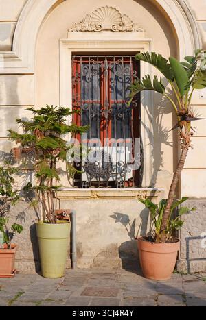 potted plants in front of an old building with air conditioner on the window, Milazzo, Sicily, Italy Stock Photo