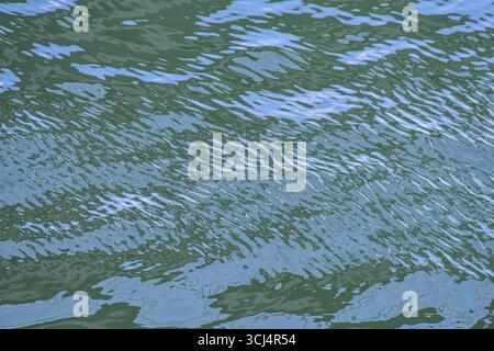 River water in daylight showing mirrored sky and gentle motion, creating serene texture perfect for natural backgrounds and designs. Stock Photo