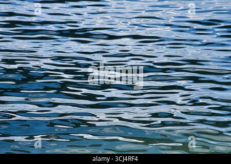 Daytime sky reflected on calm river water with soft ripples, forming abstract natural textures without visible land or shore. Stock Photo