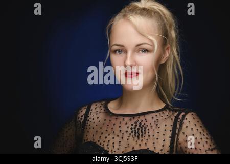 Beautiful emotional blond woman with luxury make-up in black elegant dress looking at camera smiling Stock Photo