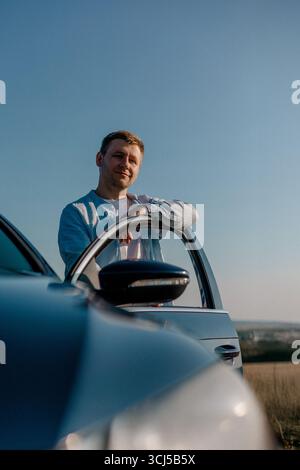 Man leaning on car door under blue sky Stock Photo