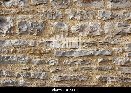 Wall of horizontally aligned gray stones held together with brown cement. Front view. Stock Photo