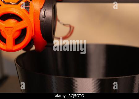 A 3D printer is poised above a dark, glossy bowl, showcasing advanced technology in action. The printer's nozzle and extruder hint at the innovative d Stock Photo