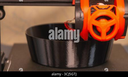 A 3D printer is engaged in the process of crafting a sleek black bowl, showcasing advanced technology and innovation in a contemporary workshop enviro Stock Photo