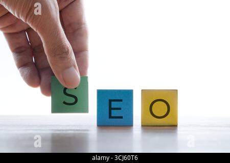 A hand placing a wooden block with the letter S next to letter E and O. SEO or search engine optimization, marketing strategy, and digital business Stock Photo