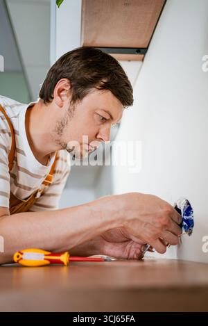 Electrician is carefully installing electrical sockets in a modern kitchen, demonstrating his expertise in home electrical work, ensuring safety and functionality Stock Photo