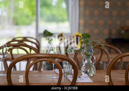Wooden served table ready for guests. Wooden decorated table with glasses, forks, napkin. Elegant dinner table with sunflower (Helianthus annuus). Stock Photo