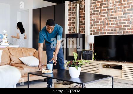 Man setting cake on table in modern living room, preparing for celebration Stock Photo