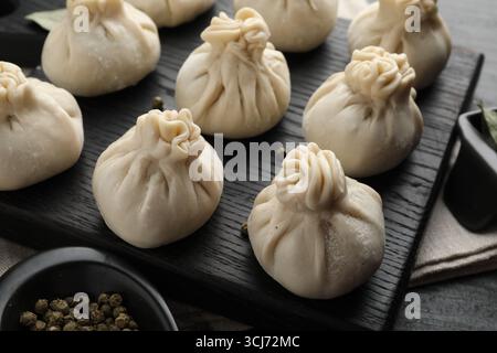 Uncooked khinkalis (dumplings) with peppercorns on black table, closeup Stock Photo