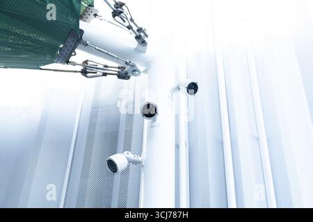 Three video cameras mounted on a white pole holding a stretched fabric roof against a white wall. Stock Photo